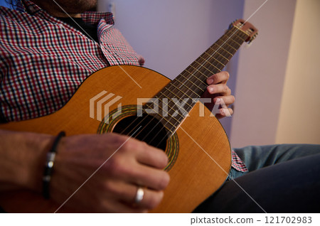 Man strumming a classical guitar in a casual indoor setting Man strumming a classical guitar in a casual indoor setting 121702983