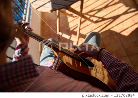 Person playing a classical guitar on a sunny tiled balcony 121702984