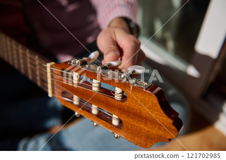 Person Tuning a Wooden Guitar Headstock in Sunlit Room Person Tuning a Wooden Guitar Headstock in Sunlit Room 121702985