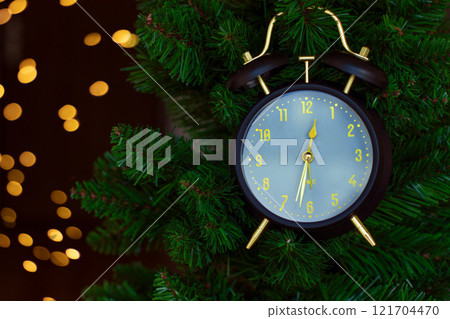 Alarm clock on a green Christmas tree, on a dark background with bokeh. 121704470