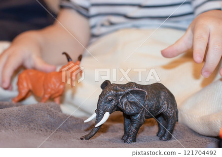 A child plays with a small black toy elephant and a toy red deer A child plays with a small black toy elephant and a toy red deer 121704492