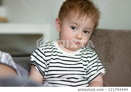 A small sick child looks sadly and tiredly with his brown eyes A small sick child looks sadly and tiredly with his brown eyes 121704494