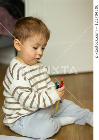 A small child draws on a book with pencils while sitting on the floor 121704506
