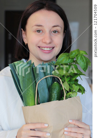 A girl with a package of green vegetables. A happy girl carries home a paper bag of greens 121704509