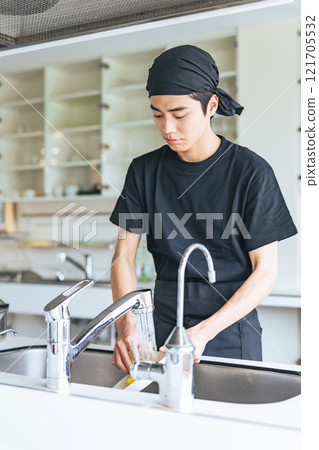 A man washing dishes in a restaurant kitchen 121705532