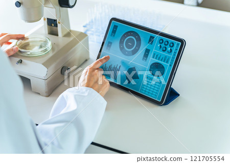 A woman in a white coat researching using a microscope and a tablet A woman in a white coat researching using a microscope and a tablet 121705554