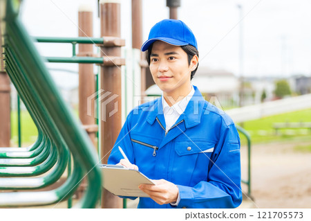 A male worker who inspects the playground equipment in the park for safety 121705573