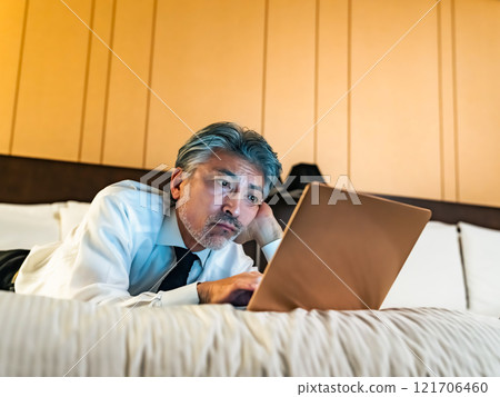 Male business person looking at a laptop computer in bed 121706460