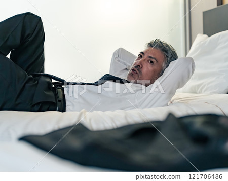 A middle-aged male business person lying on a bed in a suit A middle-aged male business person lying on a bed in a suit 121706486