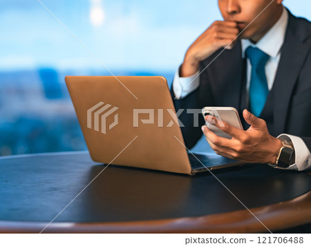 A businessman working with a laptop and smartphone in a high-rise office A businessman working with a laptop and smartphone in a high-rise office 121706488