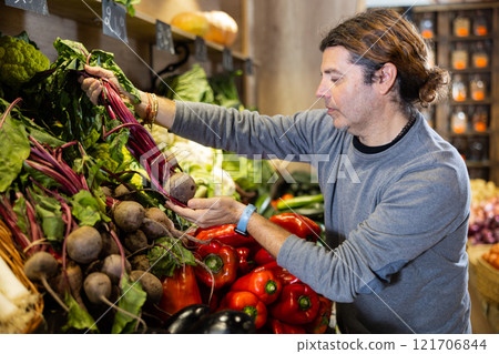 Satisfied man chooses beets in the vegetable section of supermarket 121706844