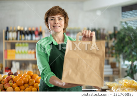 Woman seller stands in trading hall of store with goods in hand Woman seller stands in trading hall of store with goods in hand 121706883