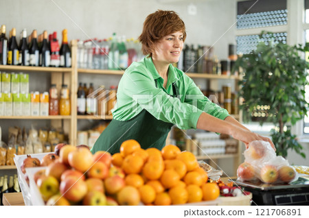 Adult woman seller weighs apples in grocery store Adult woman seller weighs apples in grocery store 121706891