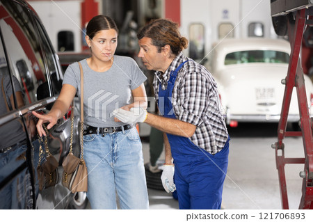 Girl showing car damages to experienced mechanic in repair workshop Girl showing car damages to experienced mechanic in repair workshop 121706893