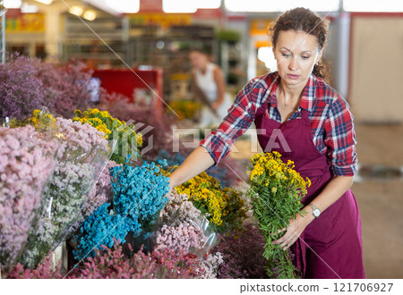 Positive female seller in apron holds dry flowers in hands Positive female seller in apron holds dry flowers in hands 121706927