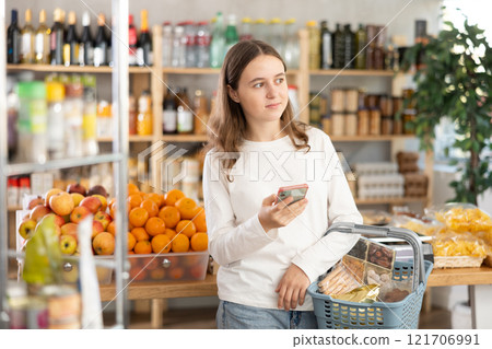 Visiting store, teen girl with phone is looking at something on shelf of showcase. 121706991