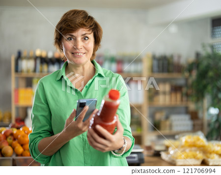 Adult woman scanning qr code of tomato juice 121706994