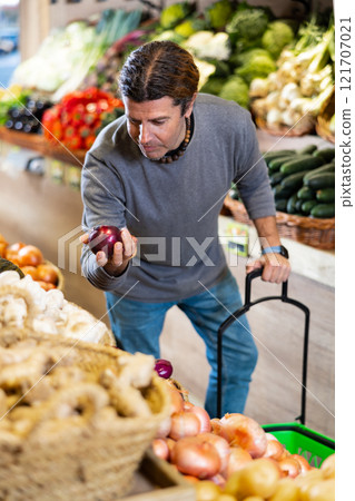Man diligently picking out red onion to buy in vegetable aisle of supermarket 121707021