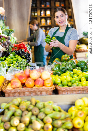 Young woman selling green capsicum in shop 121707058