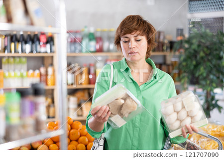 Woman holding plastic containers with oyster mushrooms and champignons, thinking about buying 121707090