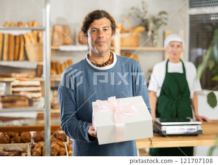 Positive man bought cake in bakery, packed in white elegant box with pink bow Positive man bought cake in bakery, packed in white elegant box with pink bow 121707108