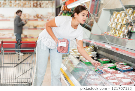 Woman looking for packaged raw sausages in grocery store 121707153