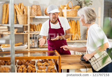 Salesman helps elderly woman choose pastries 121707158