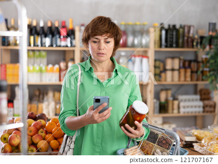Checking expiration date of canned food - female shopper scans QR code on label of pickled tomatoes using smartphone Checking expiration date of canned food - female shopper scans QR code on label of pickled tomatoes using smartphone 121707167