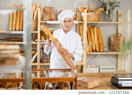 Mature female bakery employee offering bread and different baguettes for sale 121707169