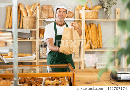 Middle-aged salesman holding paper bag in bakery Middle-aged salesman holding paper bag in bakery 121707174