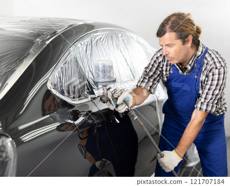 Middle aged man using spray gun to paint car in workshop Middle aged man using spray gun to paint car in workshop 121707184