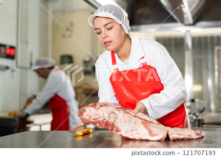 Butchery workwoman preparing raw pork ribs for packaging 121707193