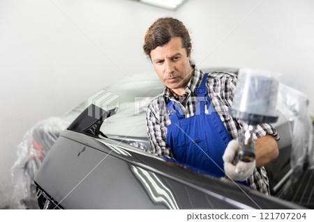 Repairman painter hand in protective glove with airbrush pulverizer painting car body 121707204