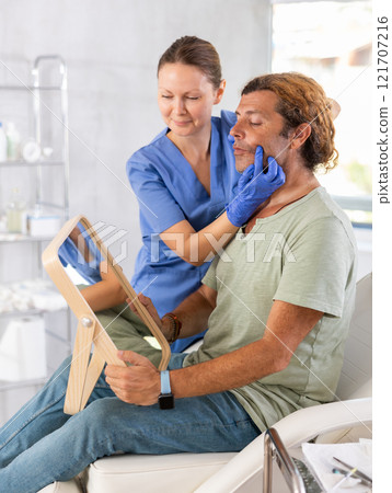 Adult patient looking at mirror during consultation of female cosmetologist 121707216