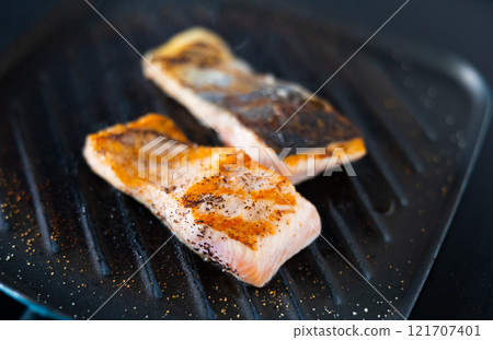 There are two pieces of broiled salmon steaks in square black frying pan 121707401