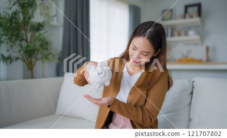 Young Asian woman putting coin in piggy bank. Save money and financial investment 121707802