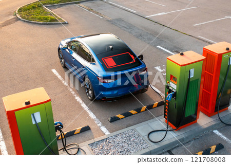 Blue electric car with flashing power indicator on roof plugged into public charging station. Vehicle receives electricity for proper work of engine 121708008