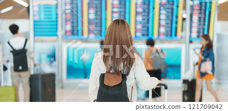 Young woman hand holding luggage handle before checking flight time in airport, Transport, insurance, travel and vacation concepts 121709042