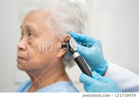 Otolaryngologist or ENT physician doctor examining senior patient ear with otoscope, hearing loss problem. 121710979