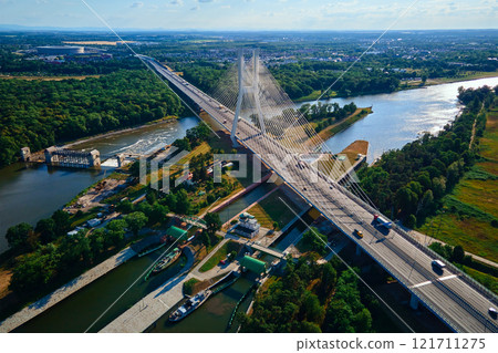 Cable-stayed bridge crossing river and canal with cars driving on sunny day 121711275