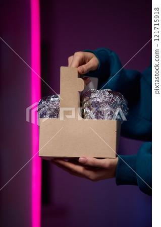 Hands holding a stylish brown paper basket that features a shiny metallic foil lid design 121715918