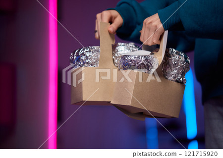 Hands holding a stylish brown paper basket that features a shiny metallic foil lid design 121715920
