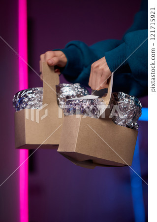 Hands holding a stylish brown paper basket that features a shiny metallic foil lid design 121715921