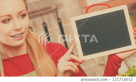 Young woman in kitchen holding blank board 121718012