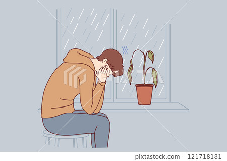 Depressed man sits alone and suffers from melancholy in room with window and wilted flower 121718181