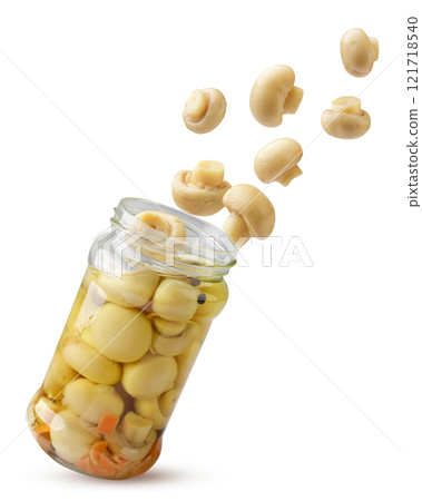 Marinated champignon mushrooms fly out of a glass jar on a white background. Isolated Marinated champignon mushrooms fly out of a glass jar on a white background. Isolated 121718540