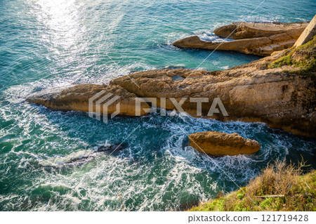 View of a sunlit rocky coastline with the sea shimmering under a clear blue sky in Ulcinj, Montenegro View of a sunlit rocky coastline with the sea shimmering under a clear blue sky in Ulcinj, Montenegro 121719428
