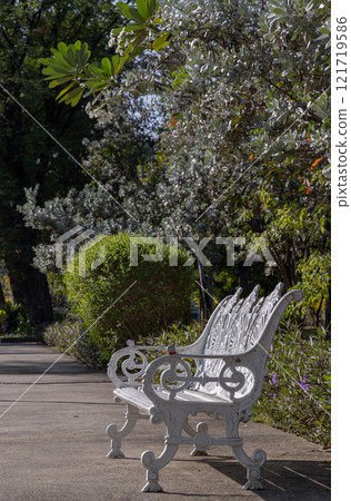 Side view of White painted cast iron victorian style garden bench with bush in the background at city park. Side view of White painted cast iron victorian style garden bench with bush in the background at city park. 121719586