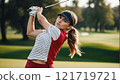 A confident female golfer swings her club on a lush green golf course, focused and poised. 121719721