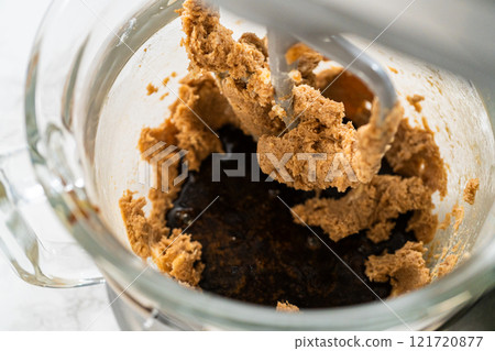 The thick, creamed mixture of butter and sugar is in the mixing bowl. The mixer paddle is beginning to fold the ingredients together, creating a cohesive blend. 121720877